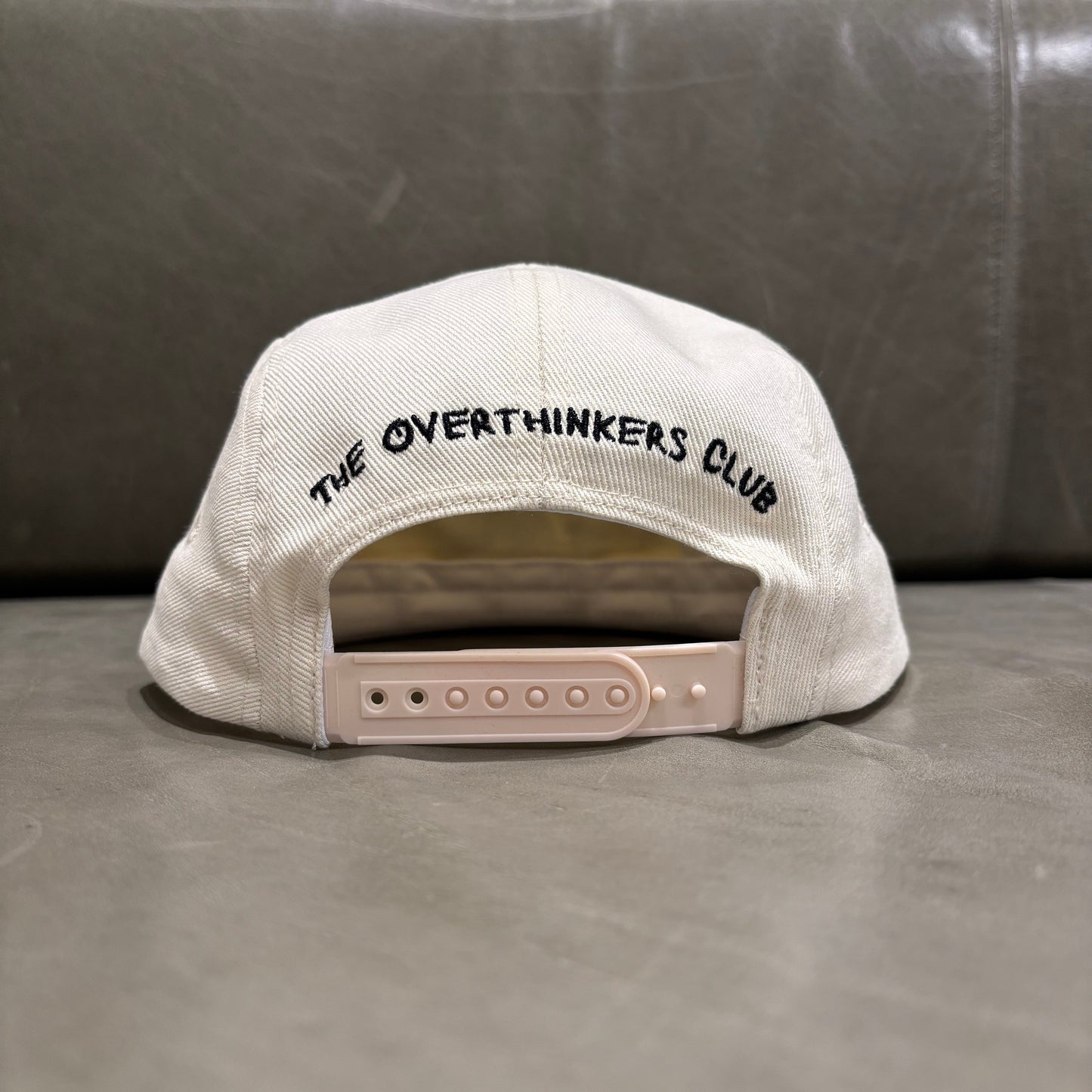 White cap with 'The Overthinkers Club' text on a gray surface