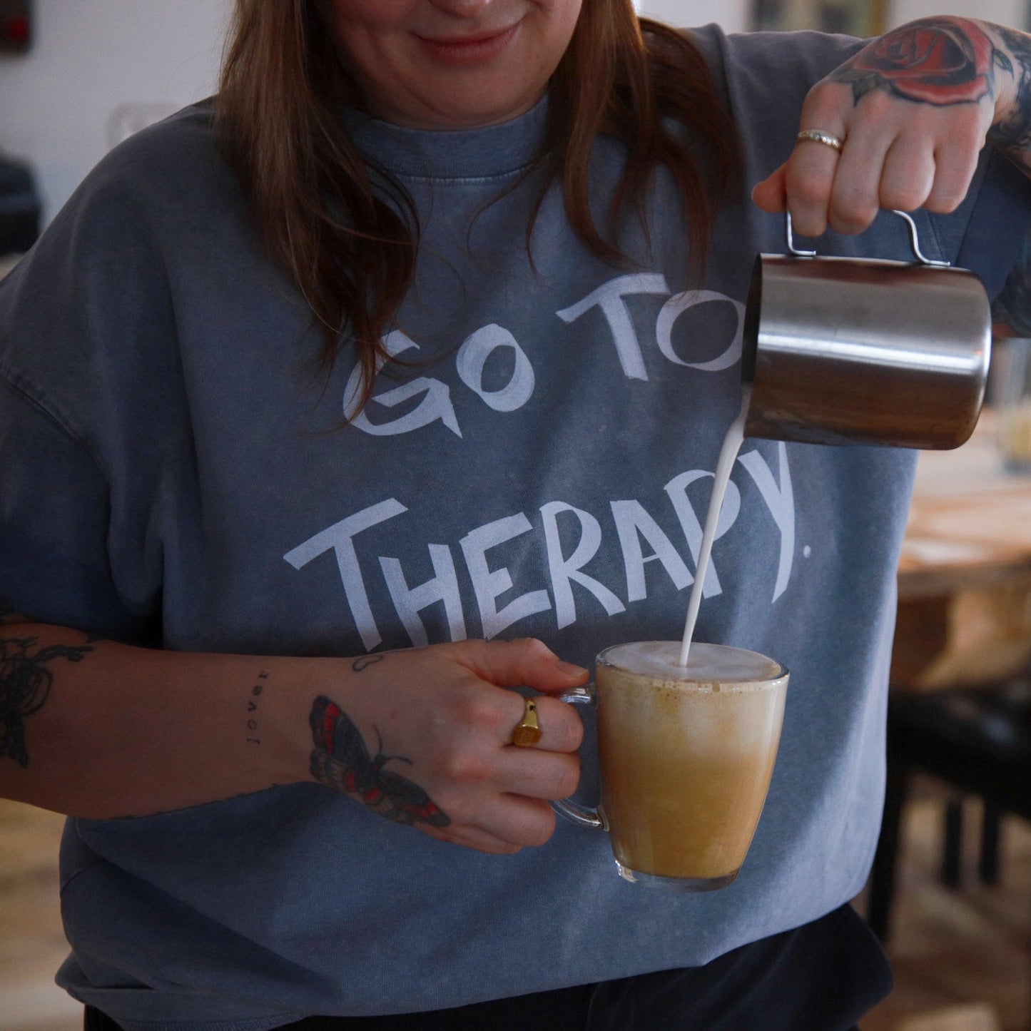 Person pouring a drink from a metal pitcher into a glass, wearing a shirt with text, in a casual setting.