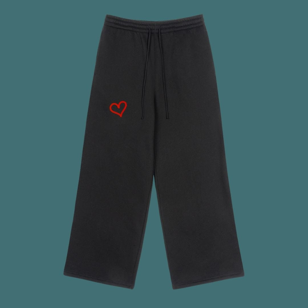 Black sweatpants with a red heart logo on a solid background