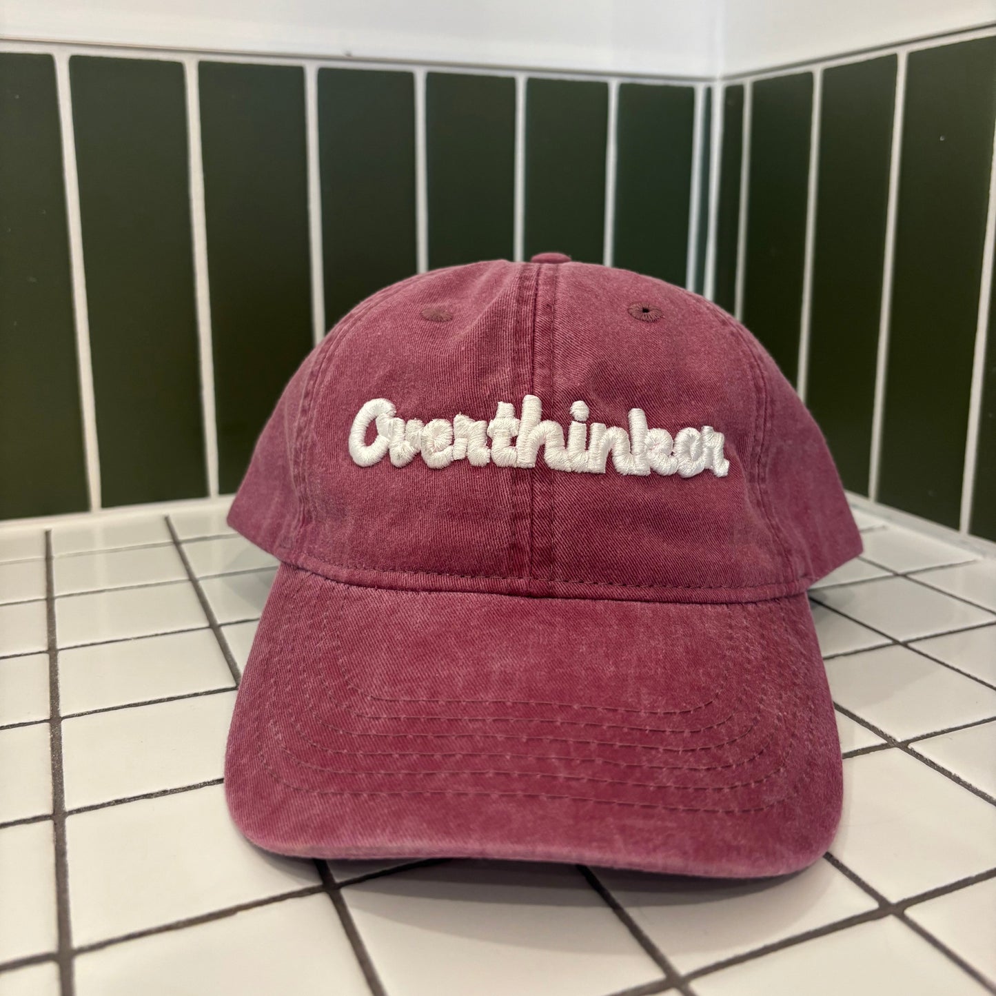 Maroon cap with 'Overthinker' text on a grid background