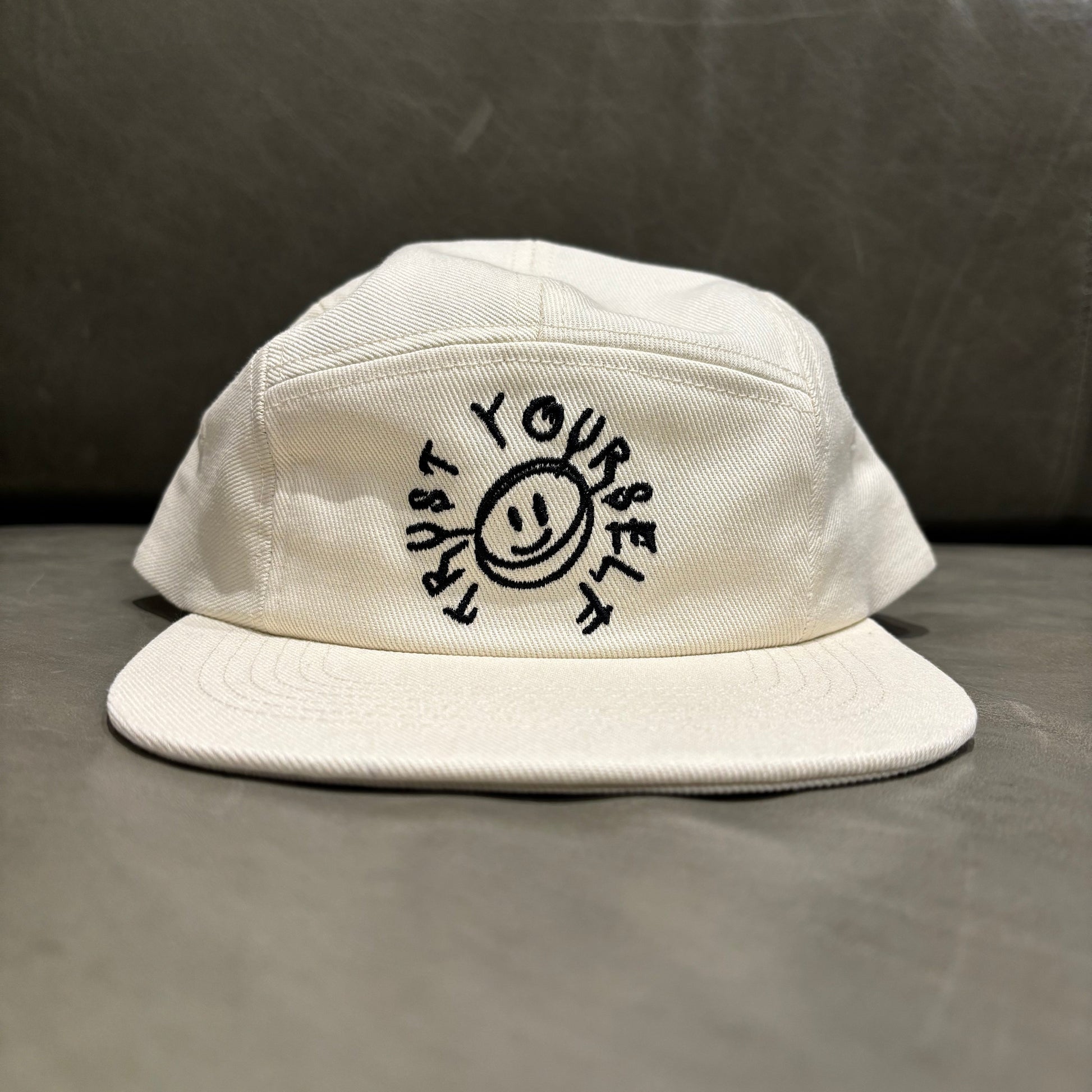 White cap with black text and smiley face design on a gray surface.