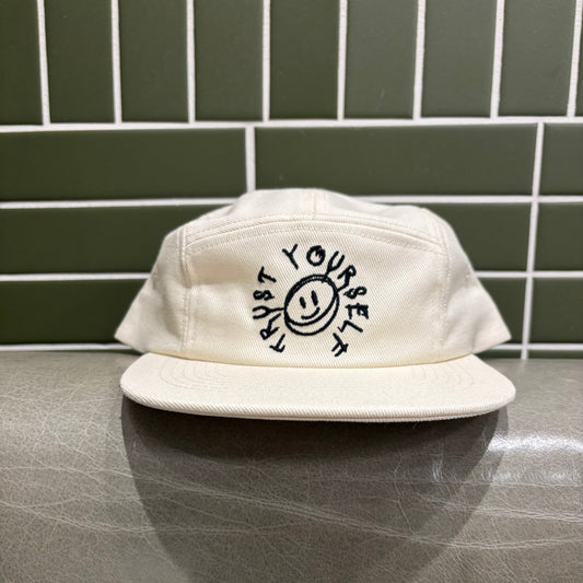 White cap with black text and smiley face design on a reflective surface with tiled wall background