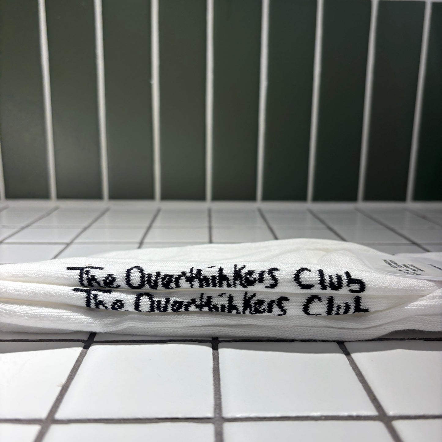 Socks with 'The Overthinkers Club' written on it, placed on a tiled surface.