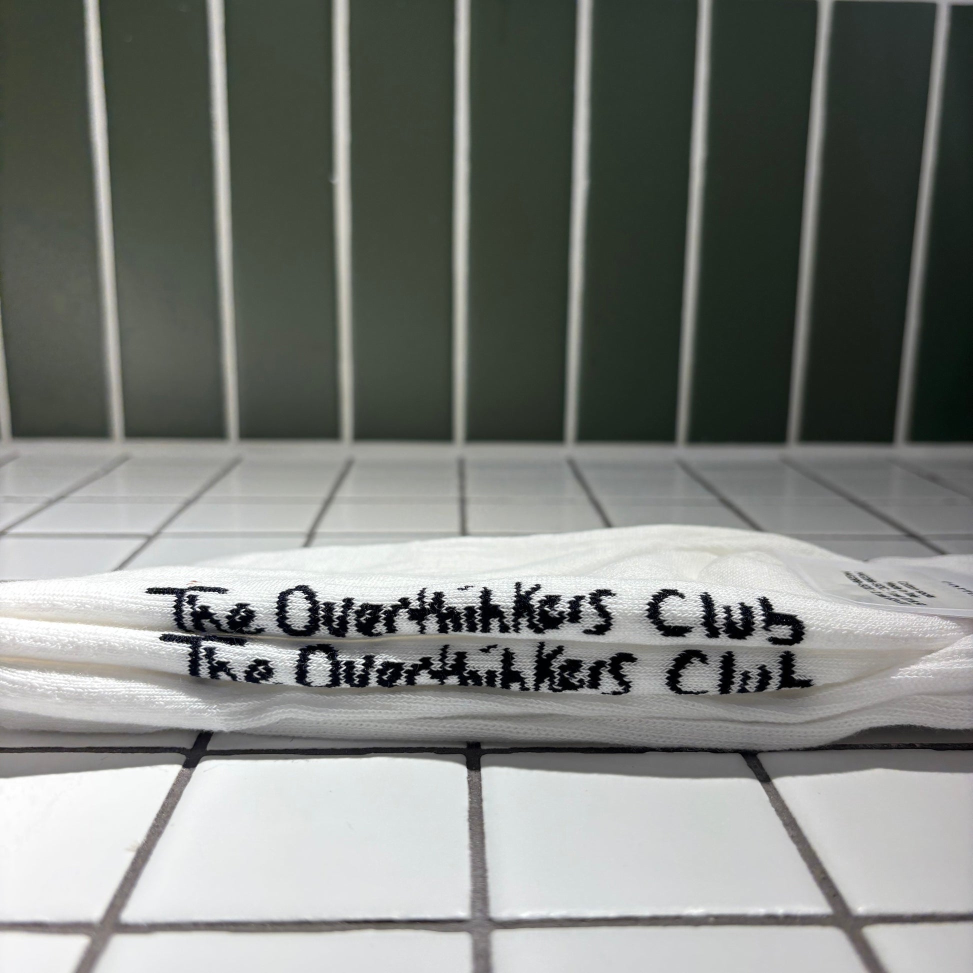 Socks with 'The Overthinkers Club' written on it, placed on a tiled surface.