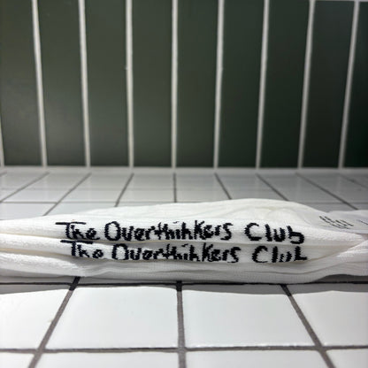 Socks with 'The Overthinkers Club' written on it, placed on a tiled surface.