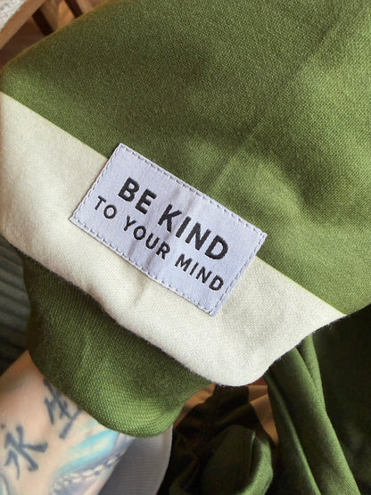 Green fabric with a label reading 'Be Kind to Your Mind' on a blurred background