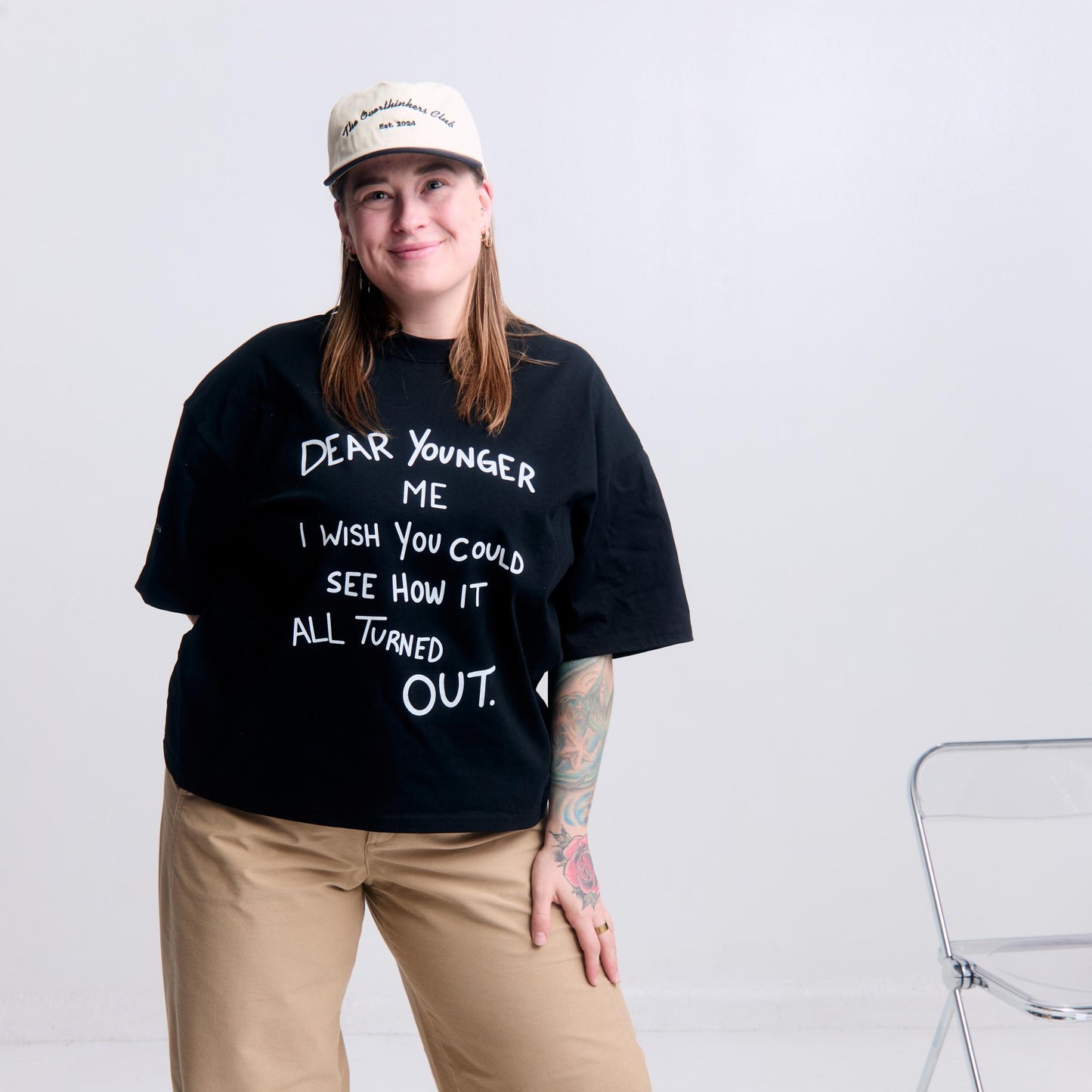 Person wearing a black t-shirt with text and a white cap, standing against a plain background.