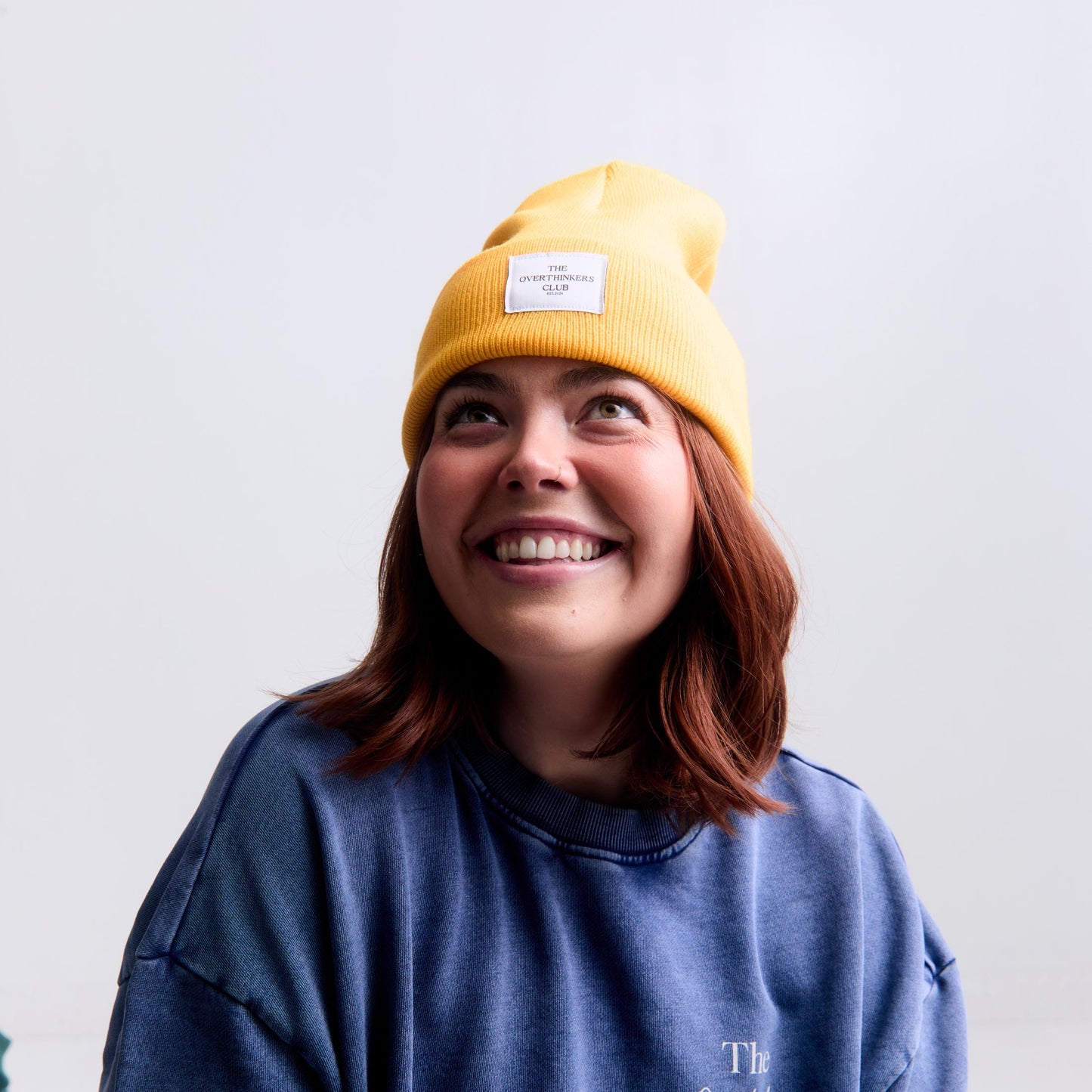 Person wearing a yellow beanie and blue sweatshirt with text on a light gray background