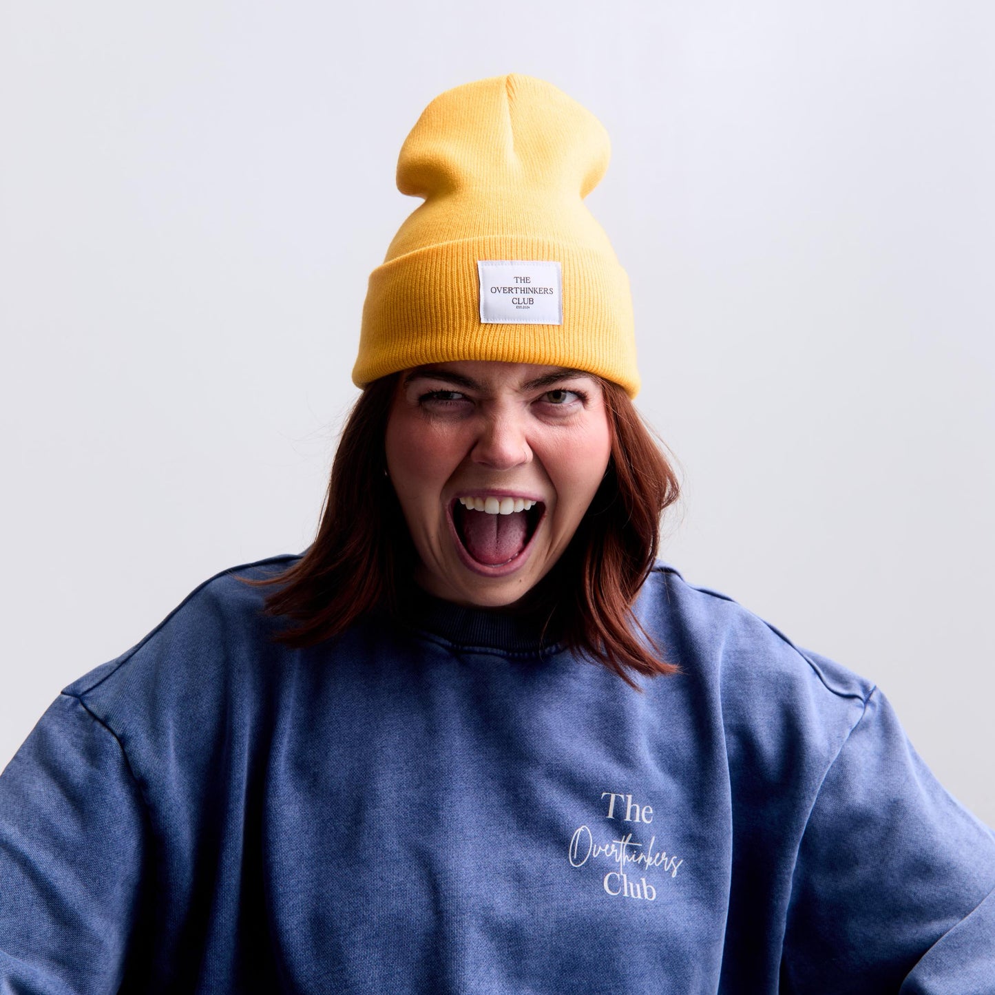 Person wearing a yellow beanie and blue sweatshirt with text on a light gray background