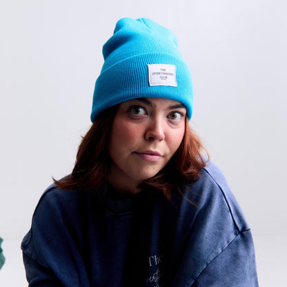Person wearing a blue beanie with a white label against a plain background