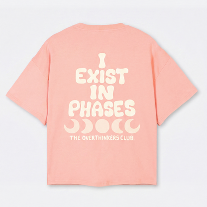 Pink t-shirt with white text 'I EXIST IN PHASES' on a light gray background